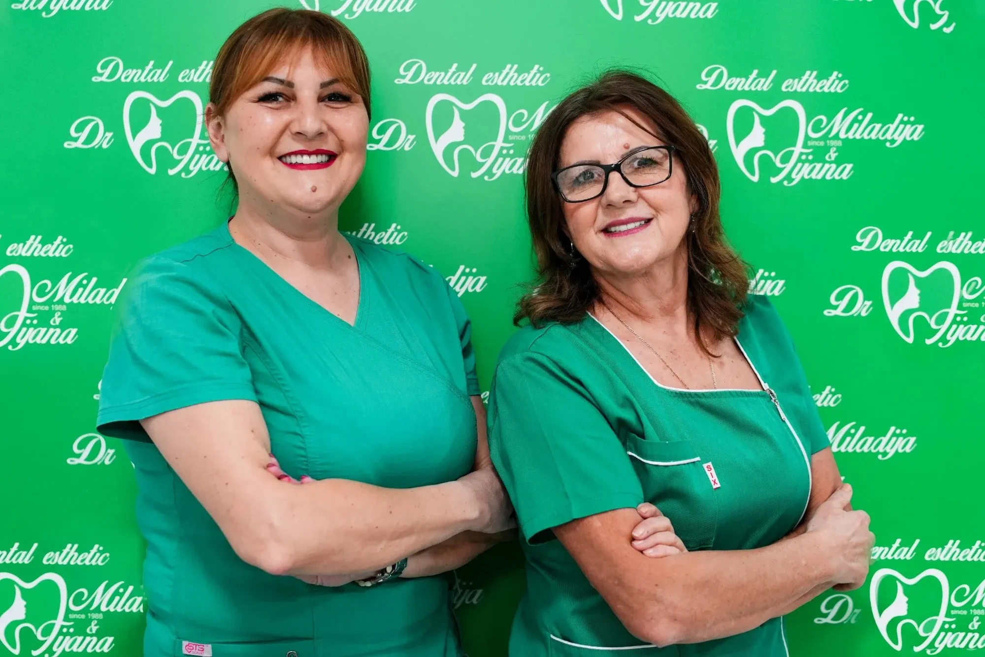 Dr Tijana Bogičević i dr Miladija Jovanović ispred zida sa logom ordinacije